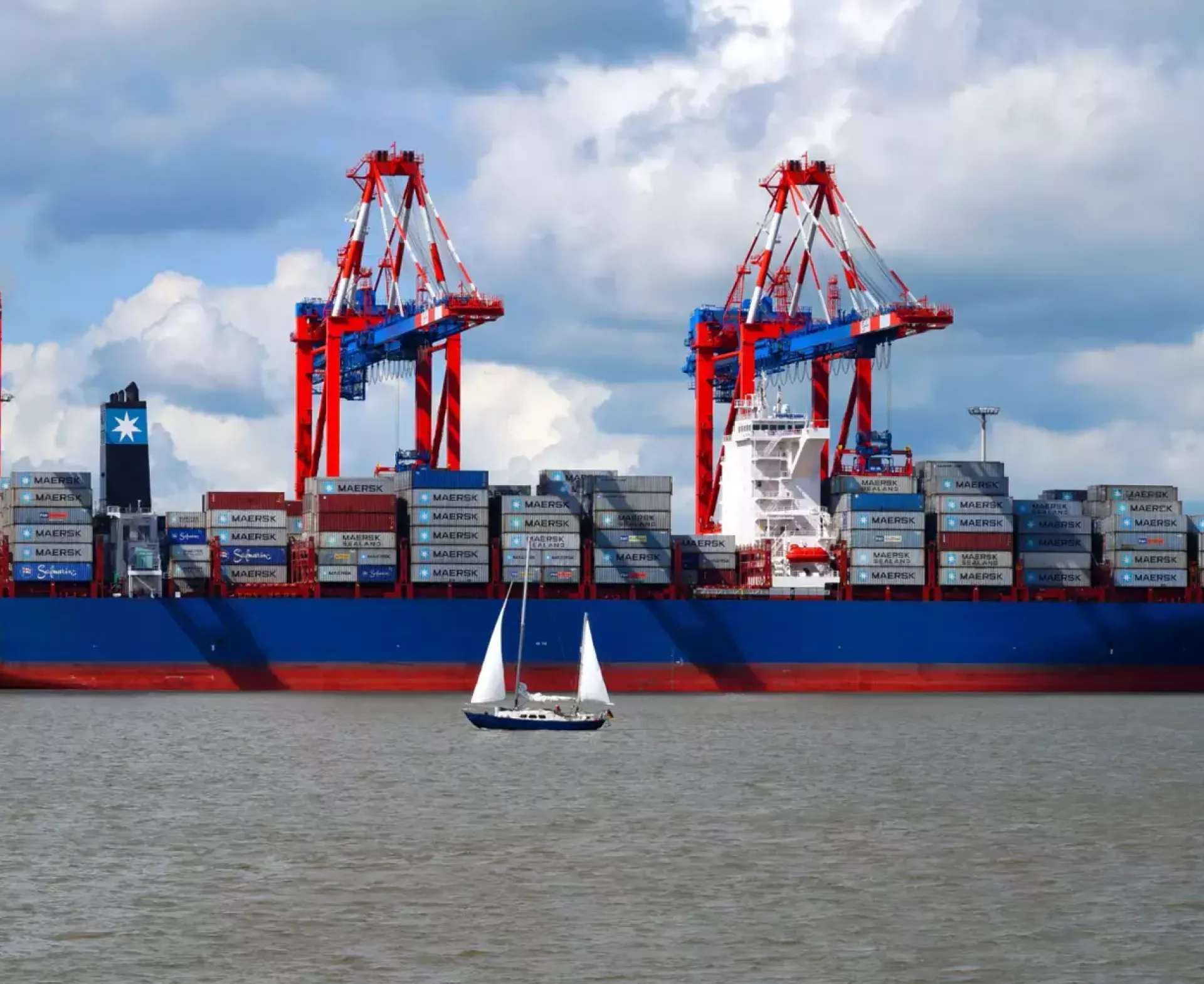 Een groot containerschip in de haven met een zeilboot op de voorgrond.