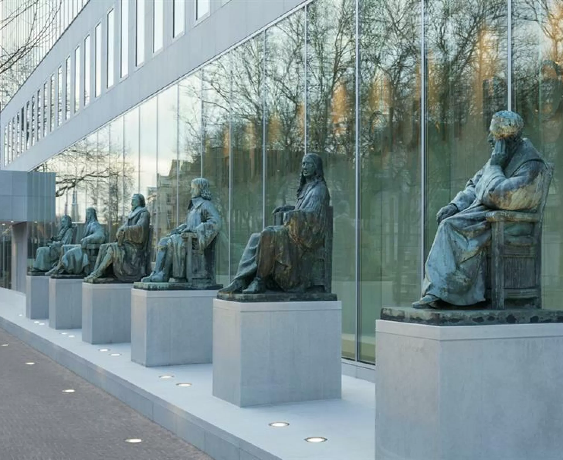 Rij van standbeelden voor een modern glazen gebouw.
