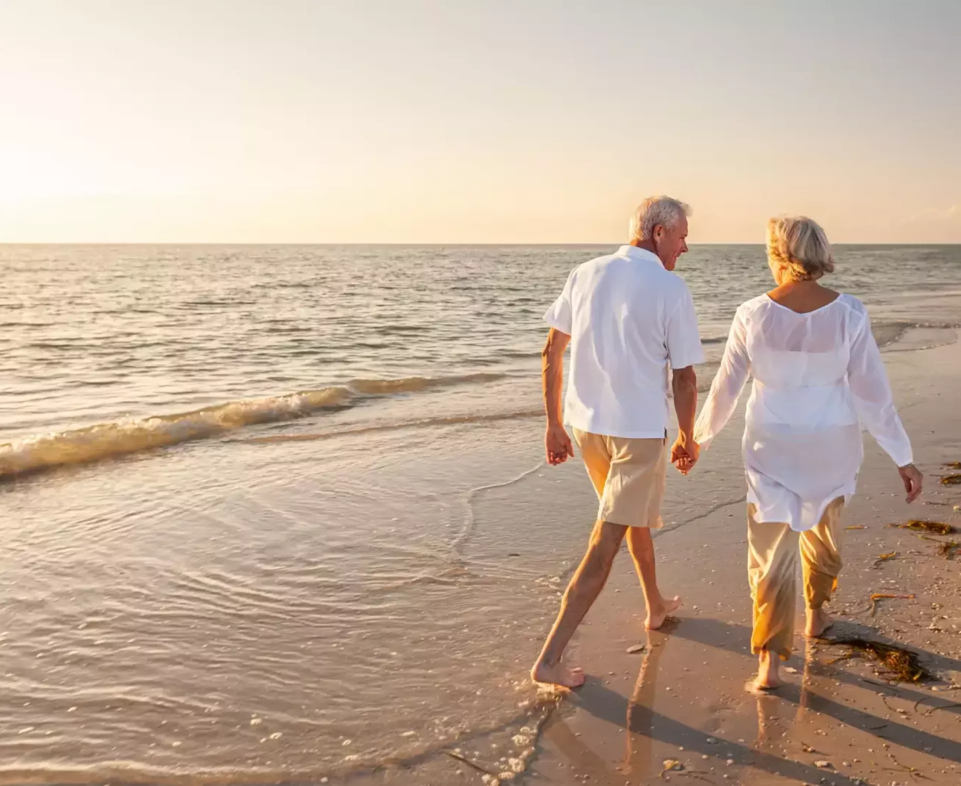 Ouder echtpaar hand in hand wandelend langs het strand bij zonsondergang.