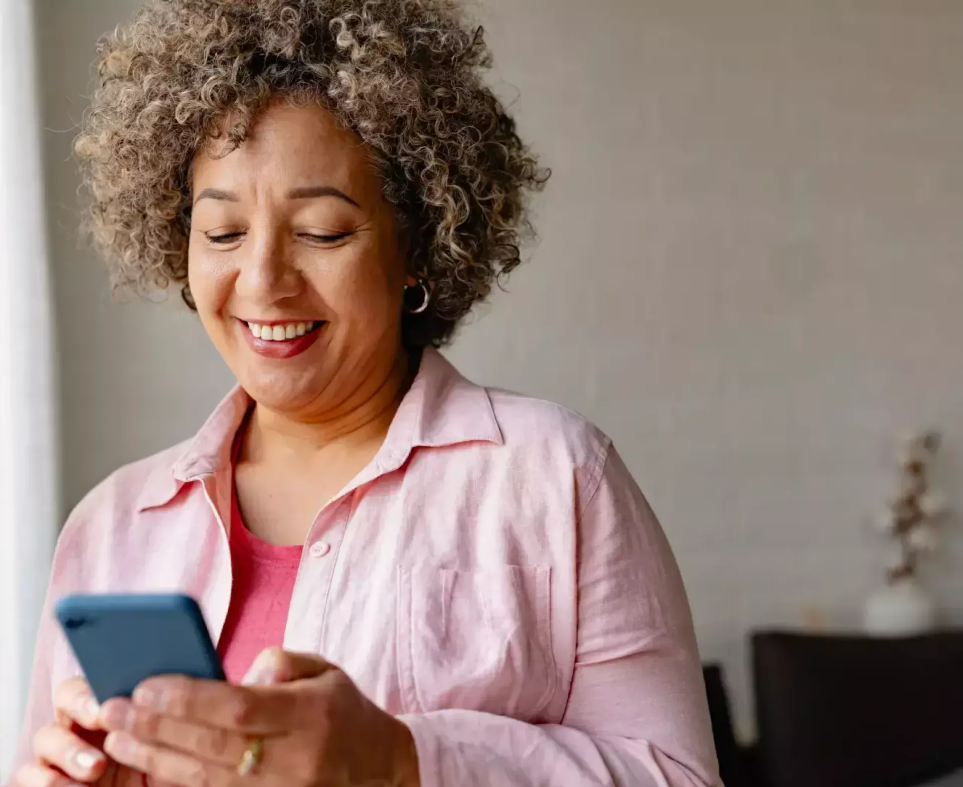 Vrouw glimlacht terwijl ze haar telefoon gebruikt bij een raam.