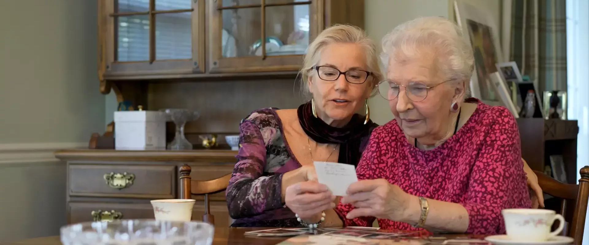 Twee oudere vrouwen bekijken samen een fotoalbum aan een tafel.