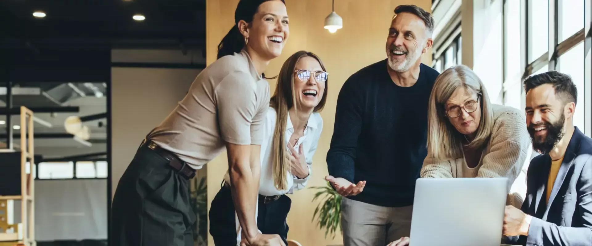 Een groep mensen lacht samen terwijl ze naar een laptop kijken.