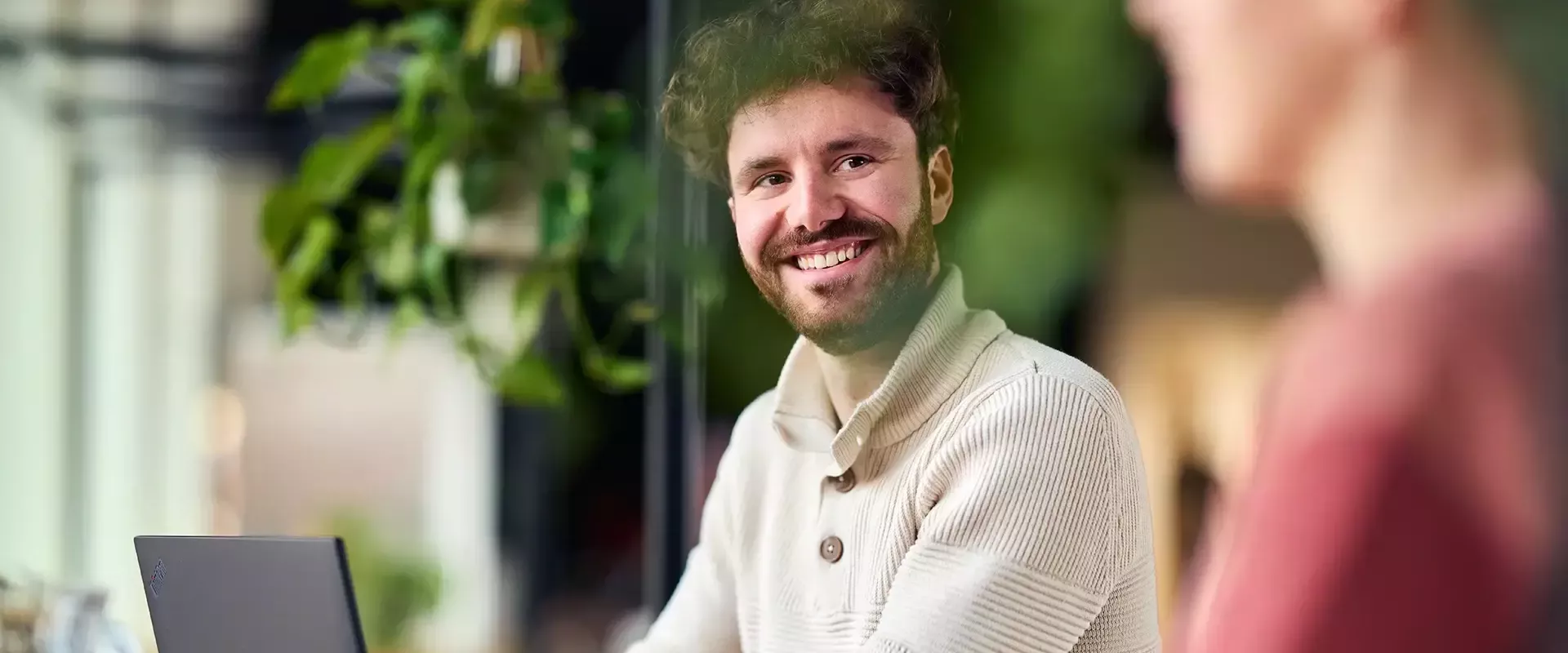 Een man glimlacht terwijl hij achter een laptop zit.
