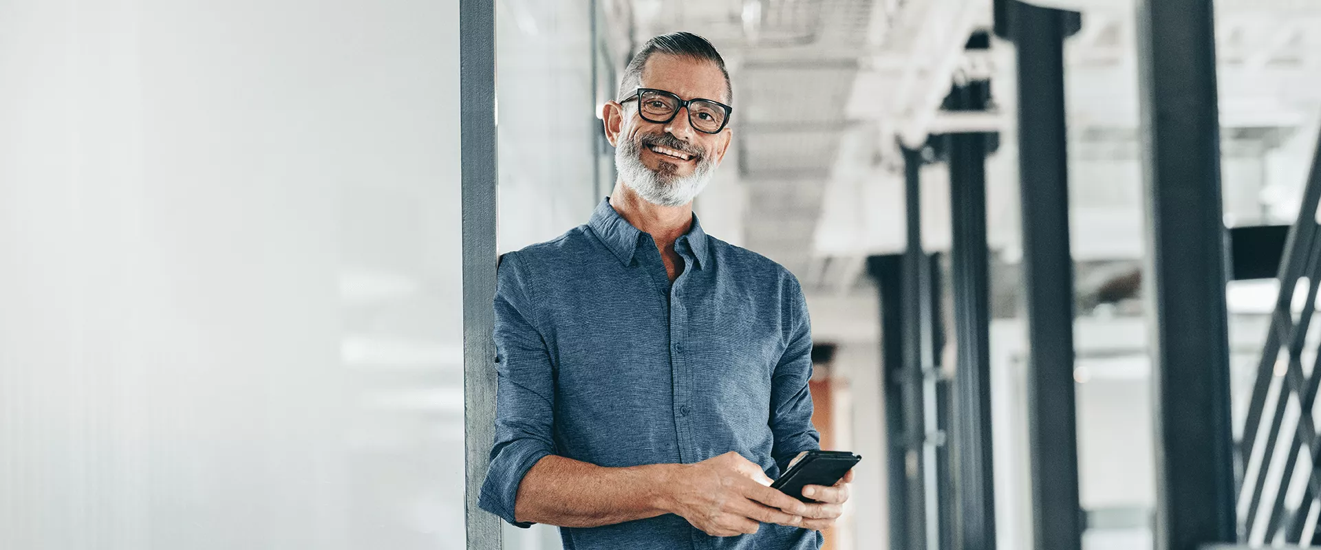 Man in een modern kantoor met een telefoon, glimlachend.