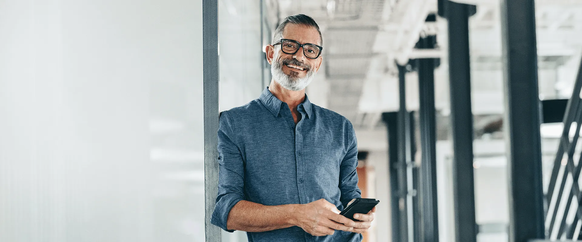 Man in een modern kantoor met een telefoon, glimlachend.