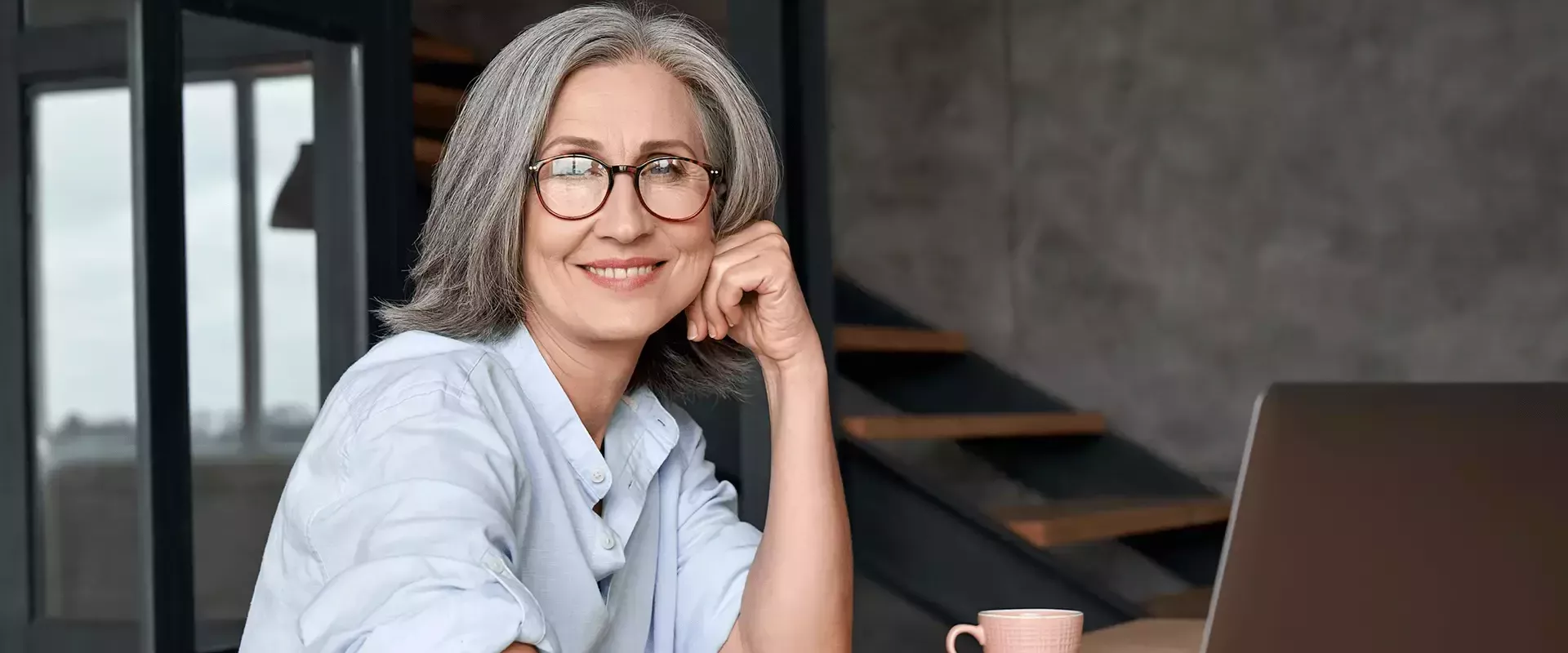 Vrouw werkt glimlachend op een laptop in een modern kantoor.