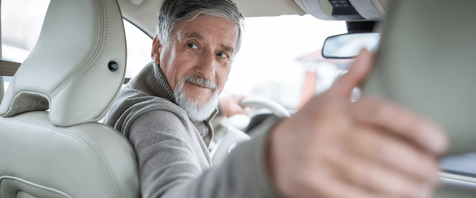 Een oudere man kijkt achterom terwijl hij in een auto zit.