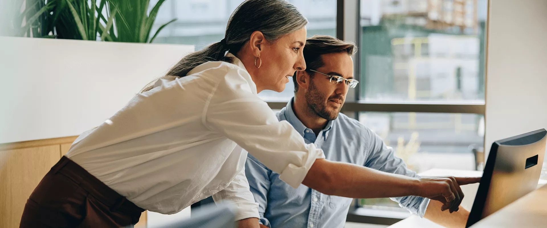 Twee collega's werken samen aan een computer in een kantoorruimte.