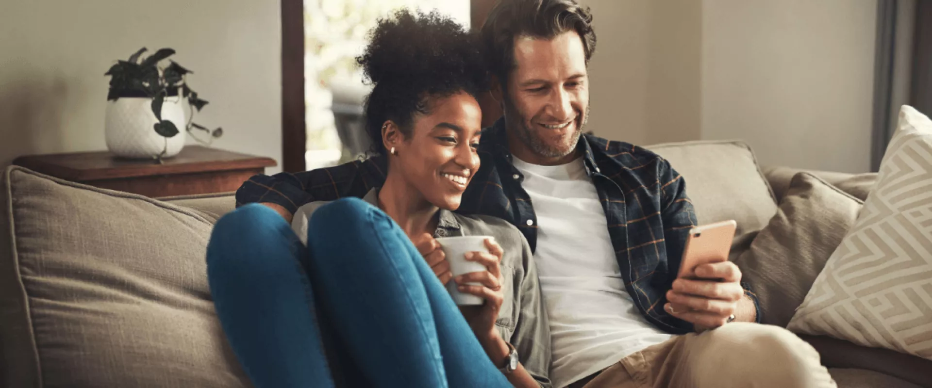 Een stel zit ontspannen op de bank terwijl ze samen naar een smartphone kijken.