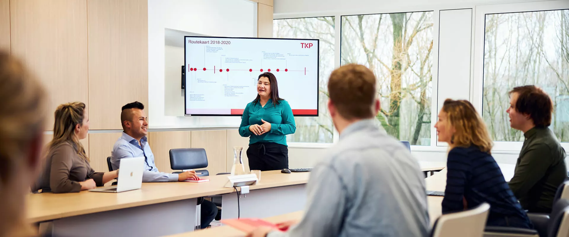 Vergadering in een conferentieruimte met presentatrice voor een scherm.