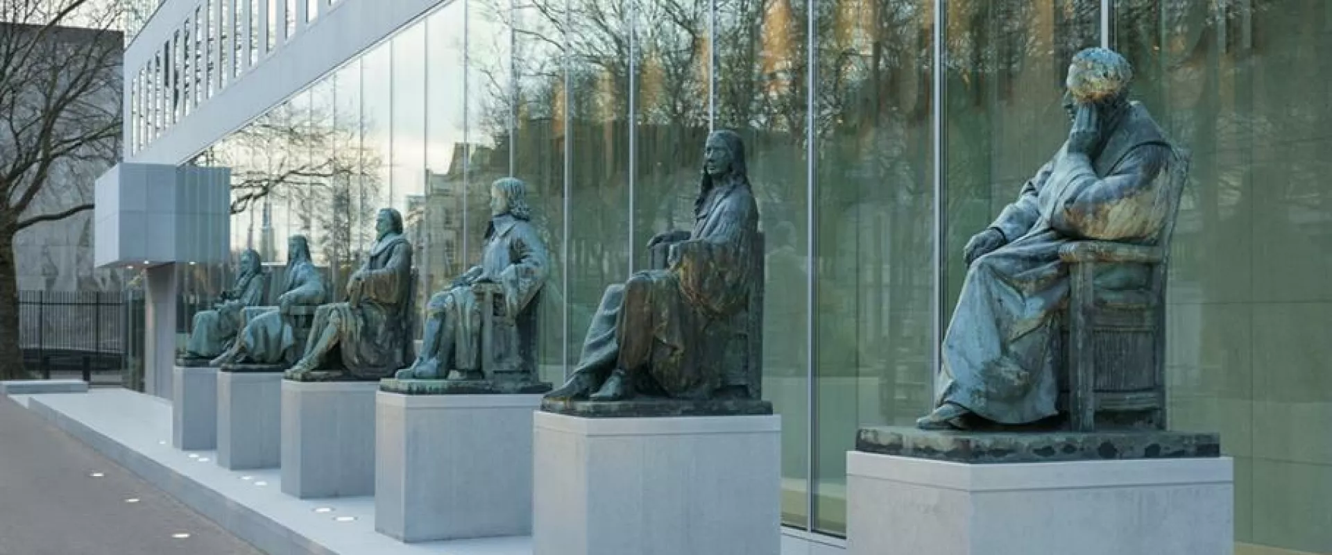 Rij van standbeelden voor een modern glazen gebouw.