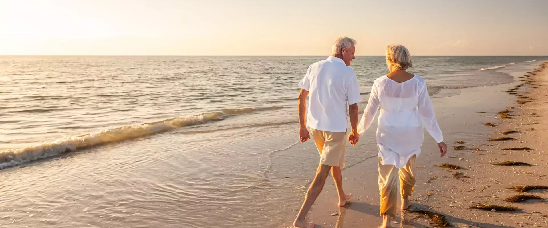 Ouder echtpaar hand in hand wandelend langs het strand bij zonsondergang.