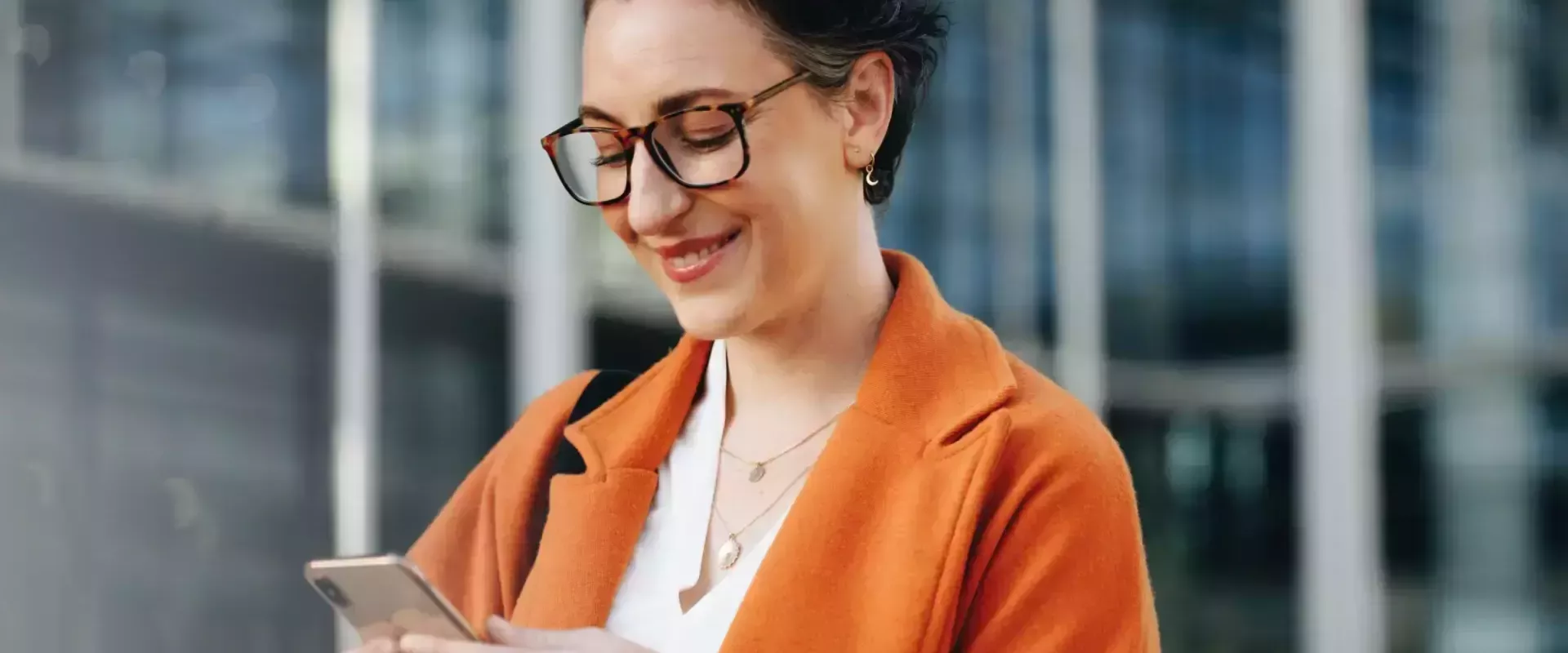 Vrouw glimlacht terwijl ze op haar telefoon kijkt.