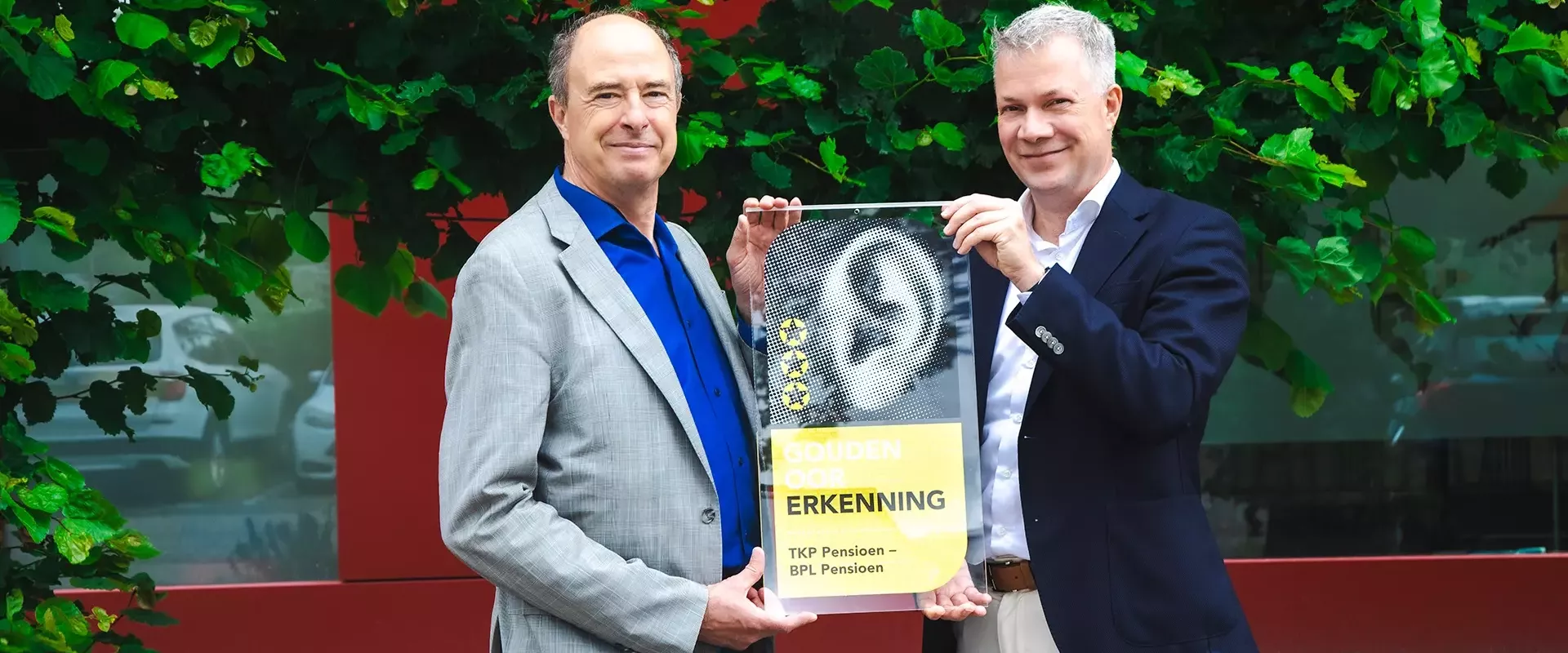 Twee mannelijke bestuurders houden de Gouden Oor Erkenning omhoog voor een groene achtergrond.