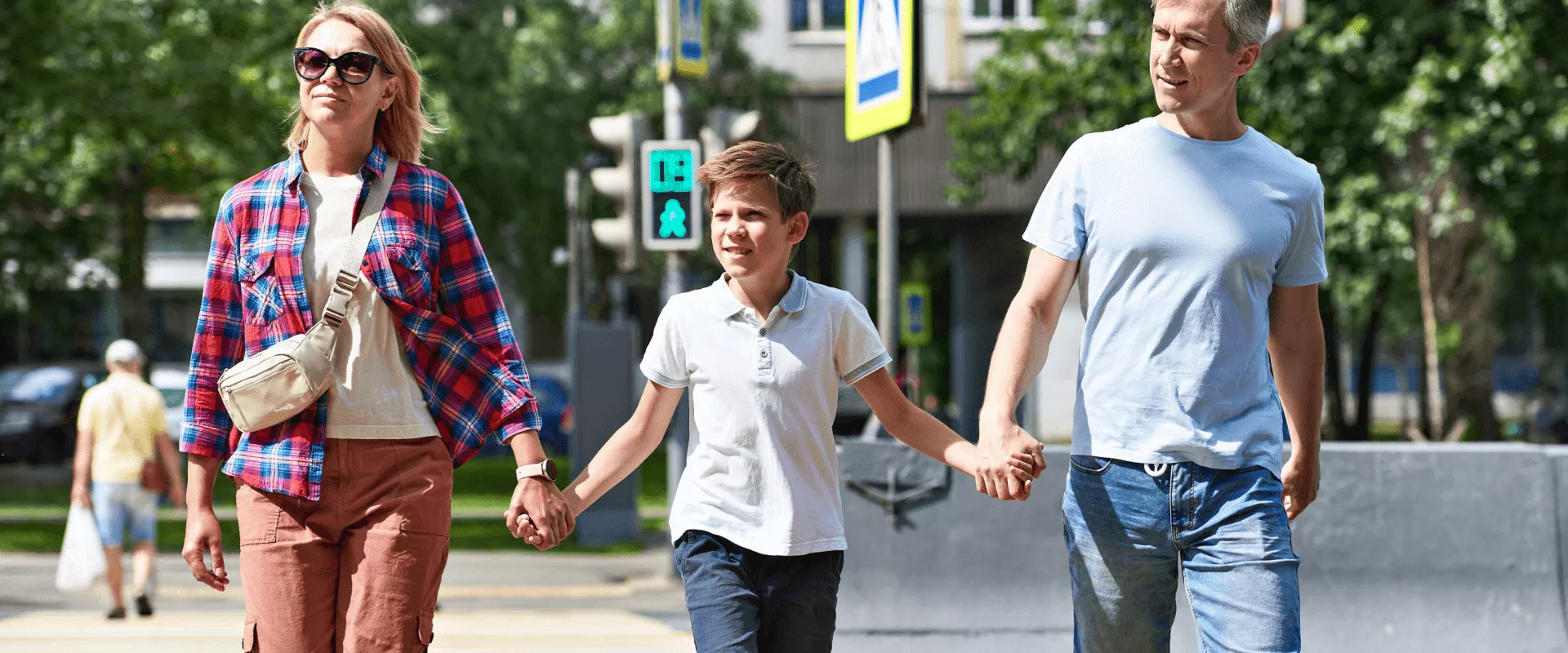 Een gezin steekt hand in hand een straat over op een zonnige dag.