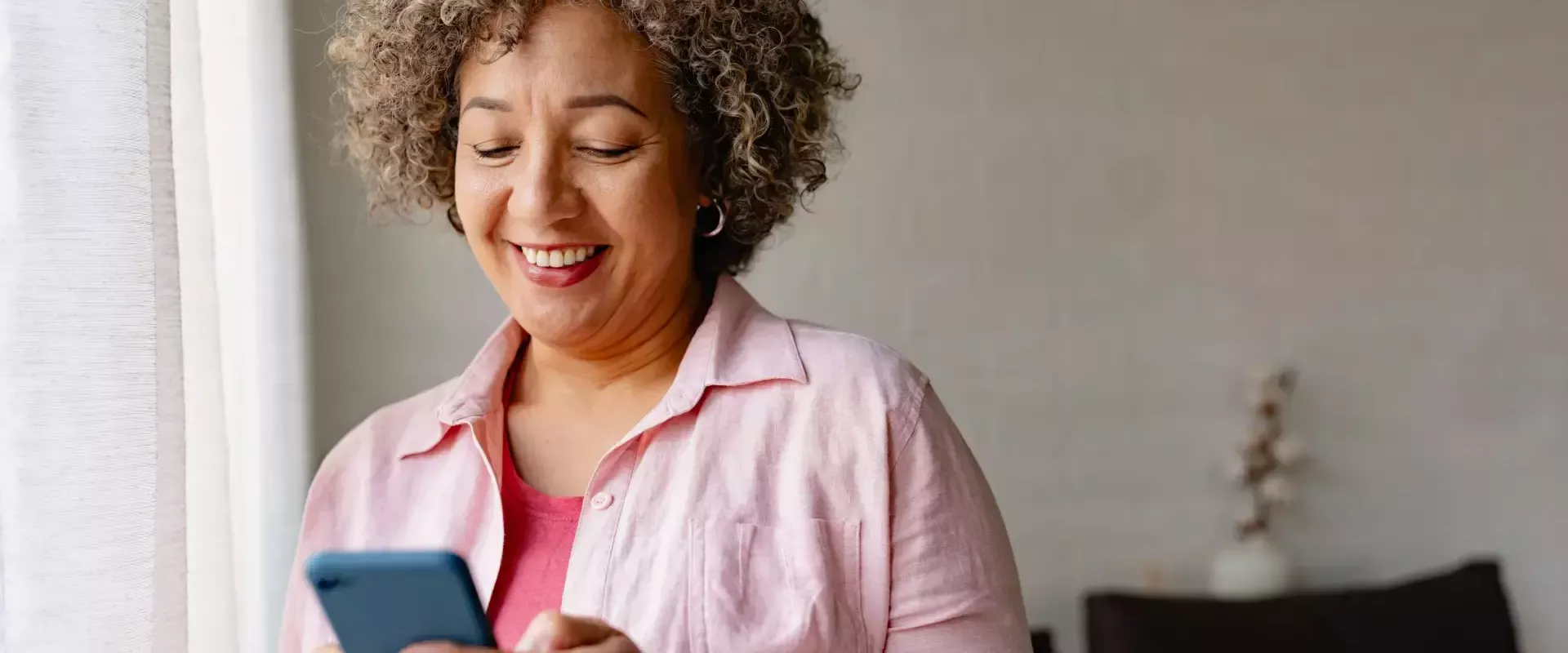 Vrouw glimlacht terwijl ze haar telefoon gebruikt bij een raam.