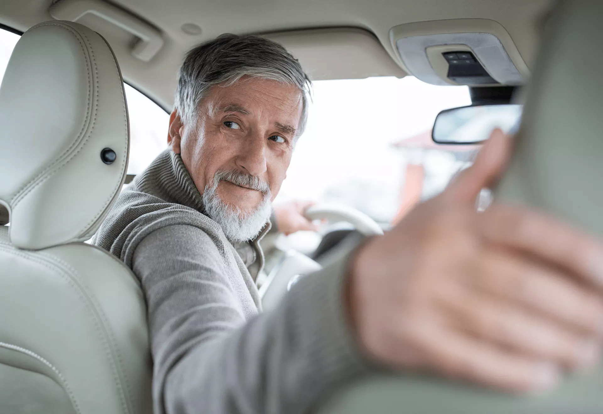Een oudere man kijkt achterom terwijl hij in een auto zit.