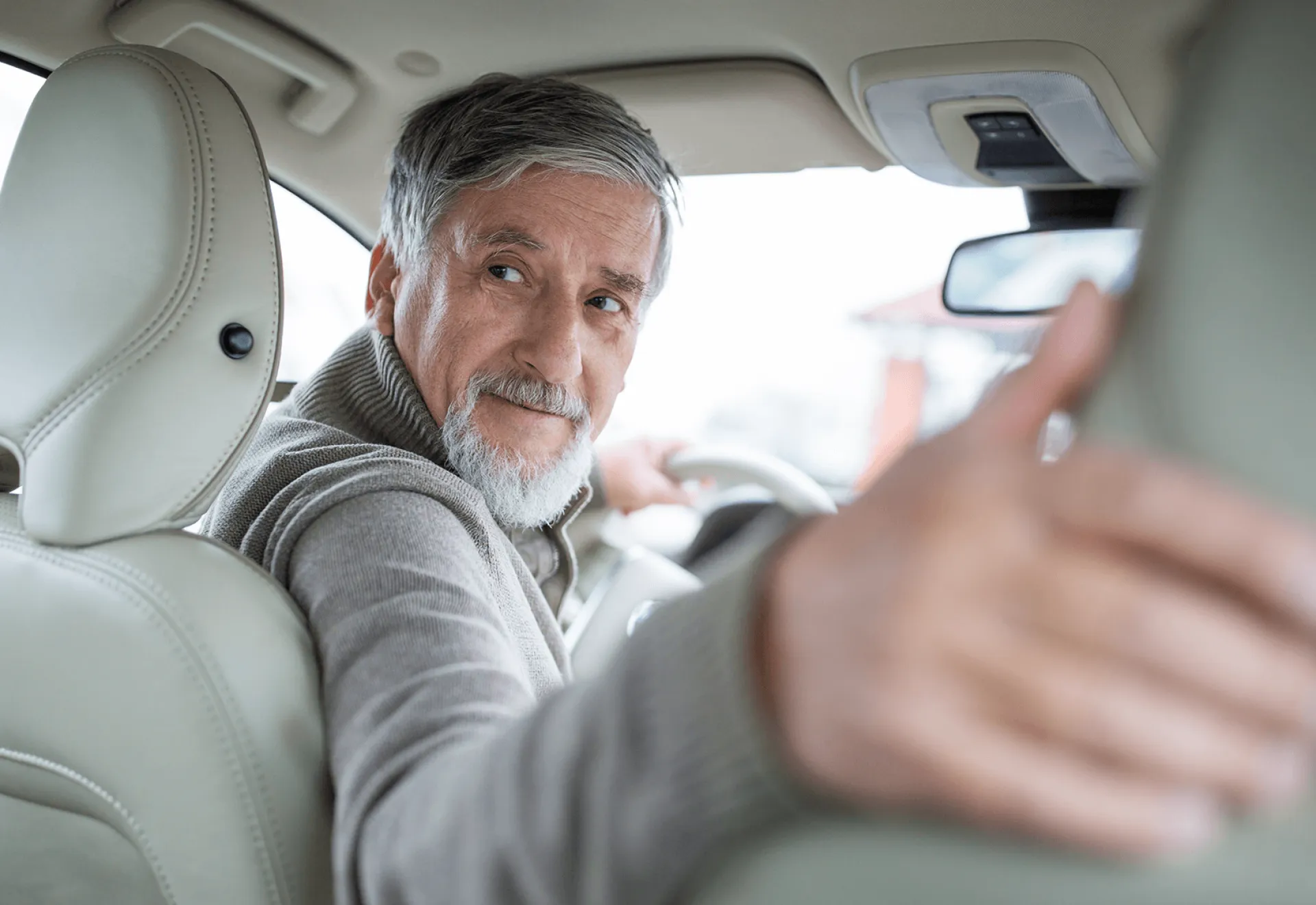 Een oudere man kijkt achterom terwijl hij in een auto zit.