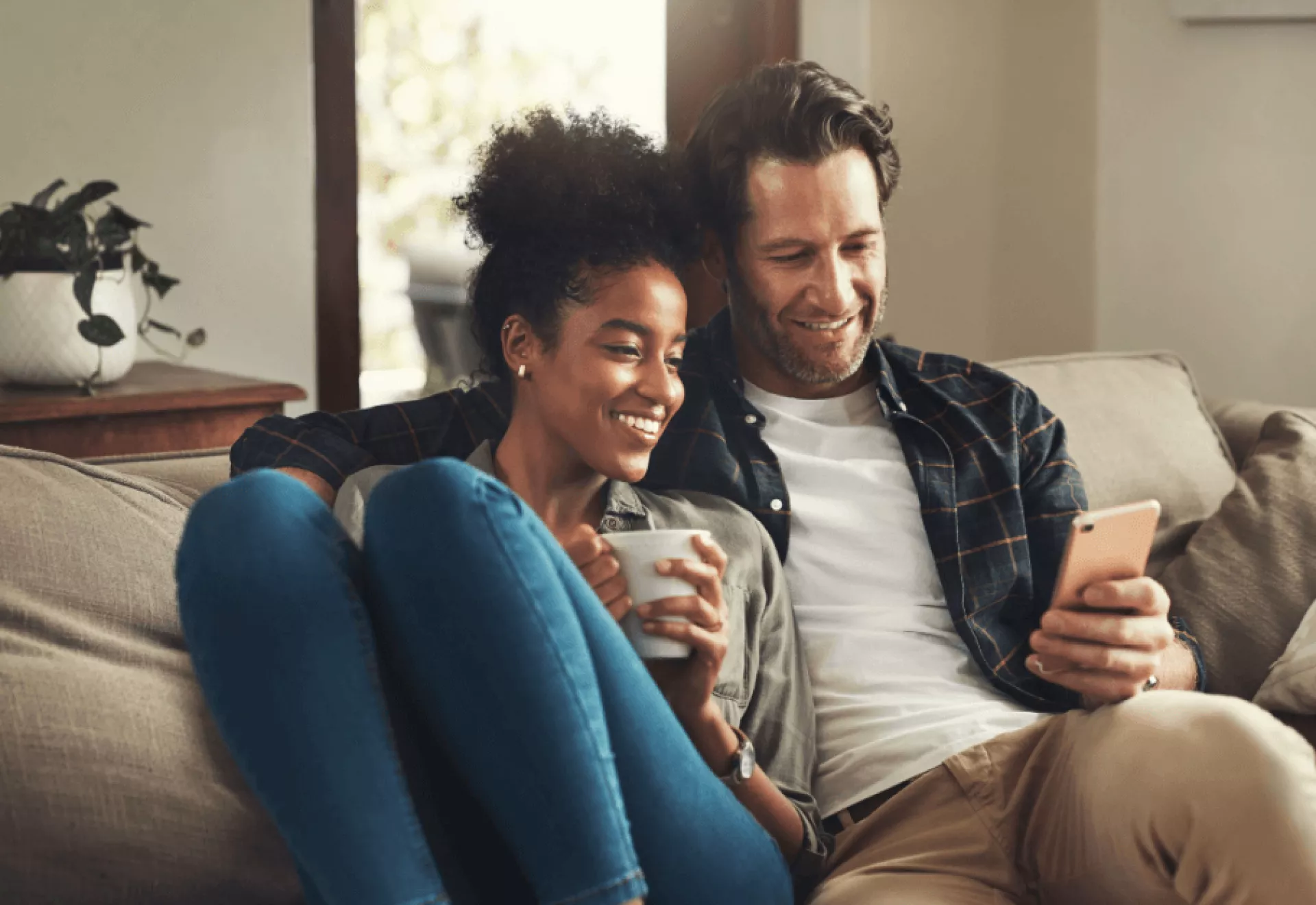 Een stel zit ontspannen op de bank terwijl ze samen naar een smartphone kijken.