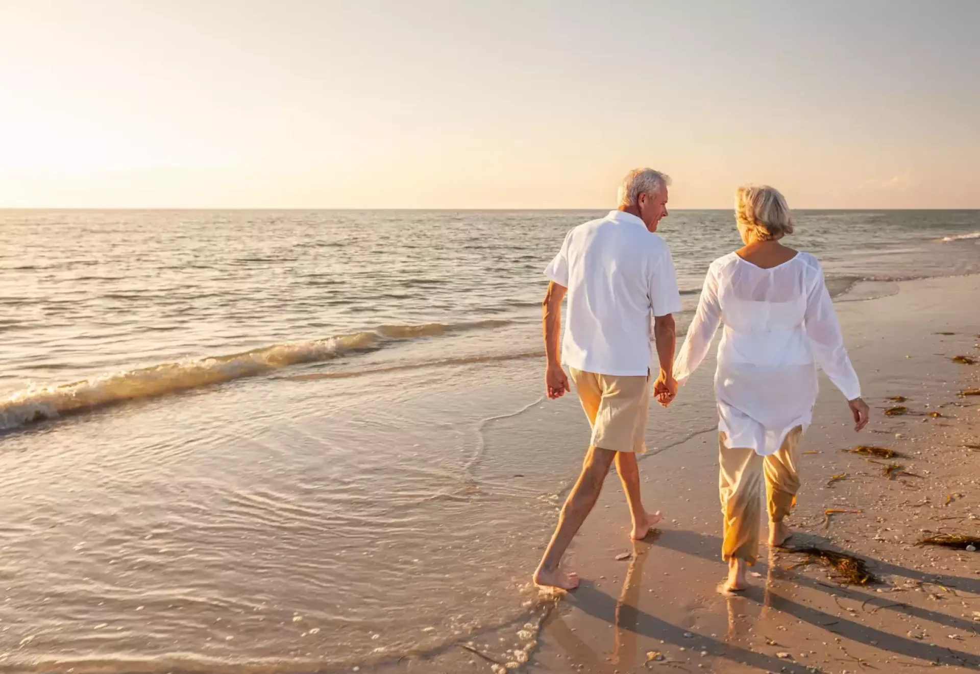 Ouder echtpaar hand in hand wandelend langs het strand bij zonsondergang.