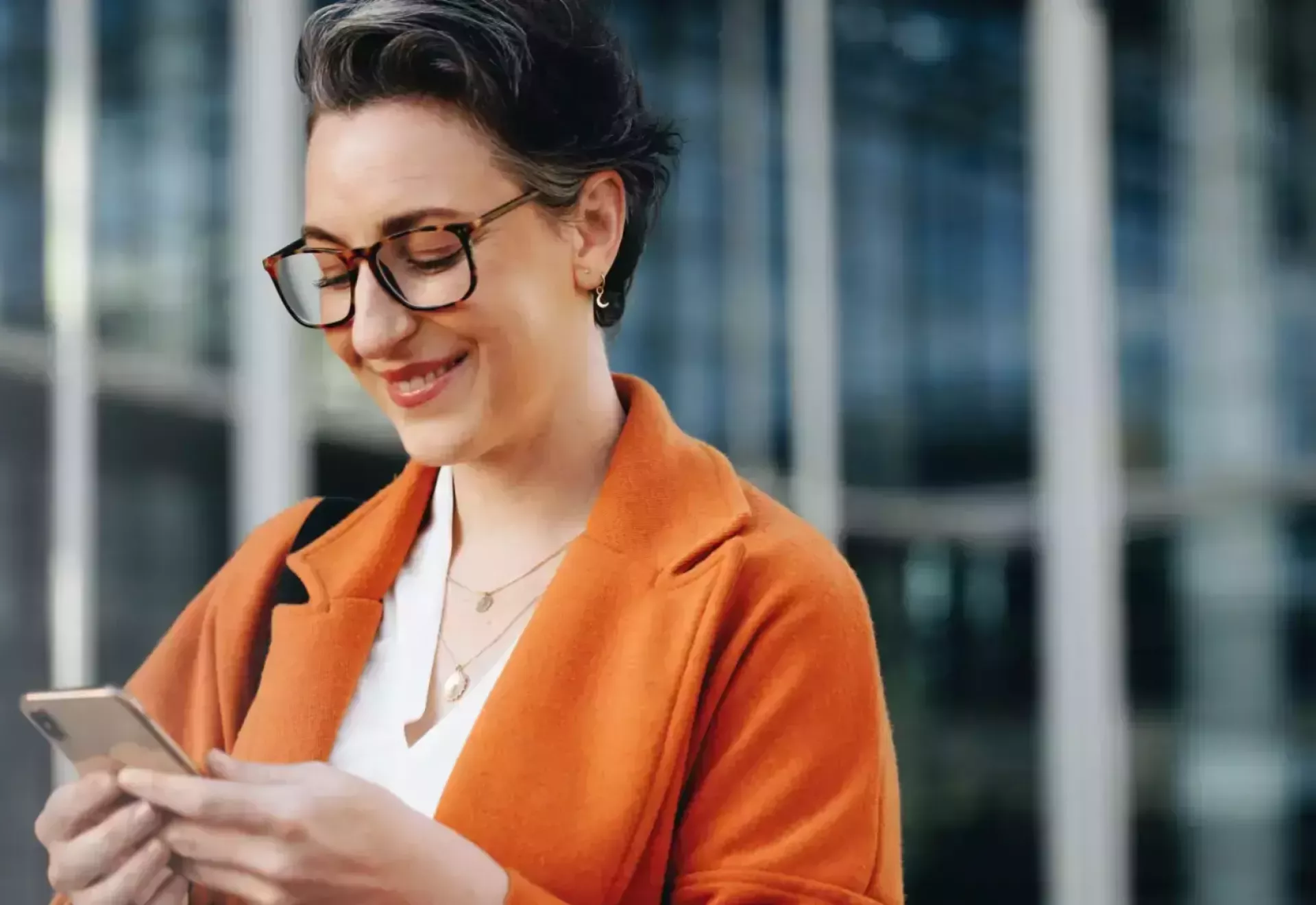 Vrouw glimlacht terwijl ze op haar telefoon kijkt.