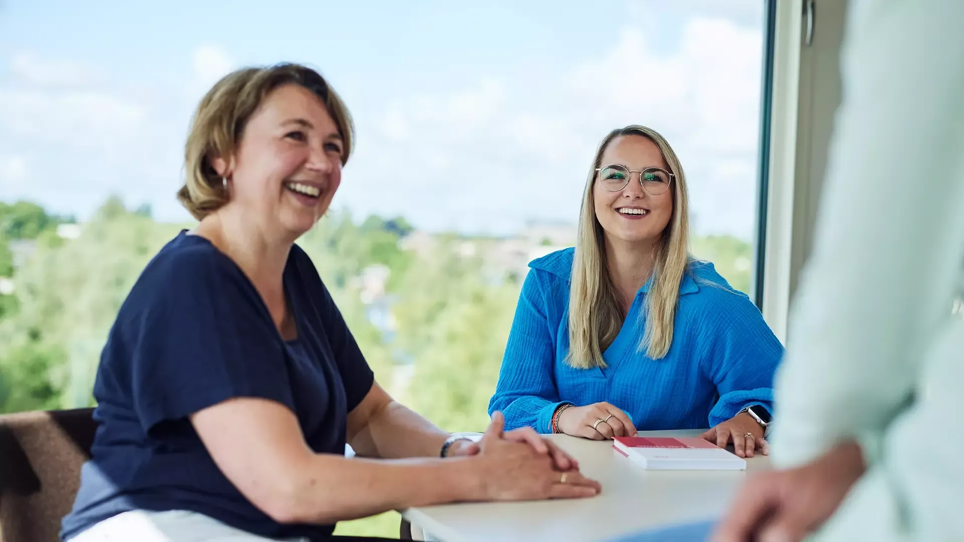 Twee vrouwen glimlachen tijdens een gesprek aan tafel.