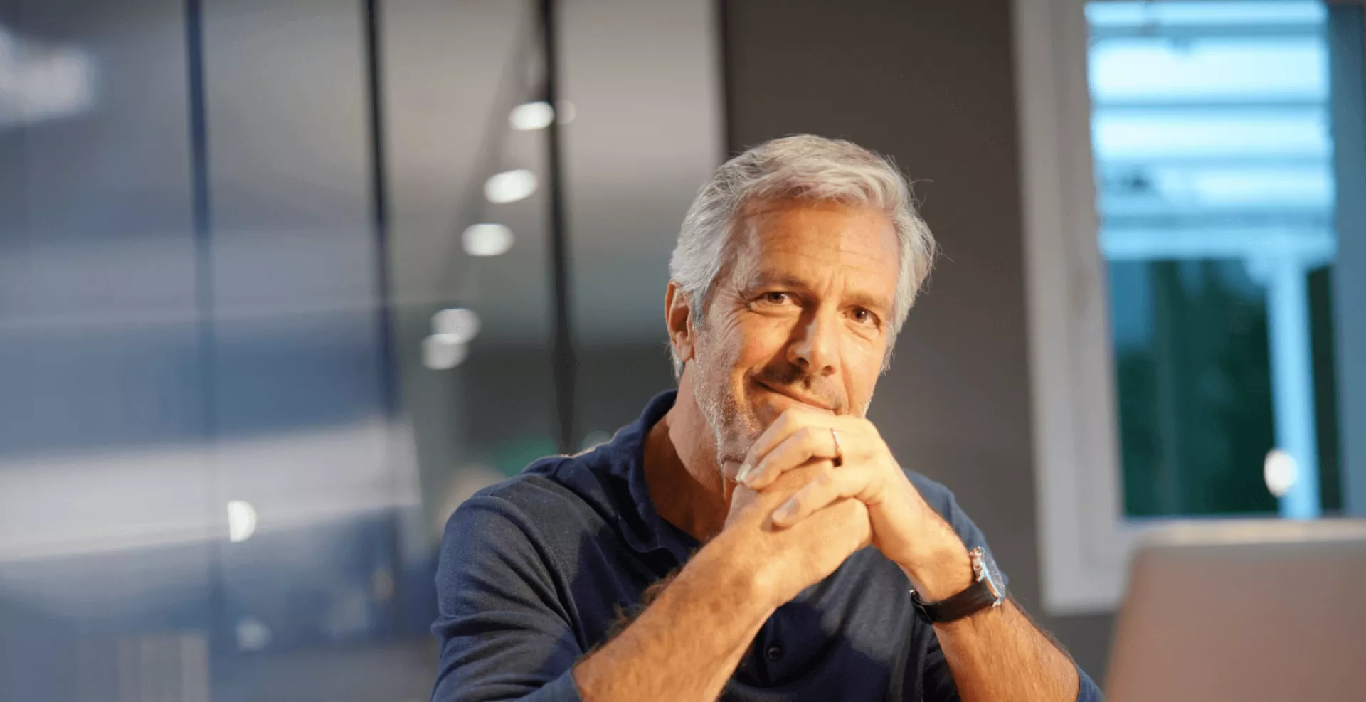 Een glimlachende man met grijs haar zittend in een moderne kantooromgeving.