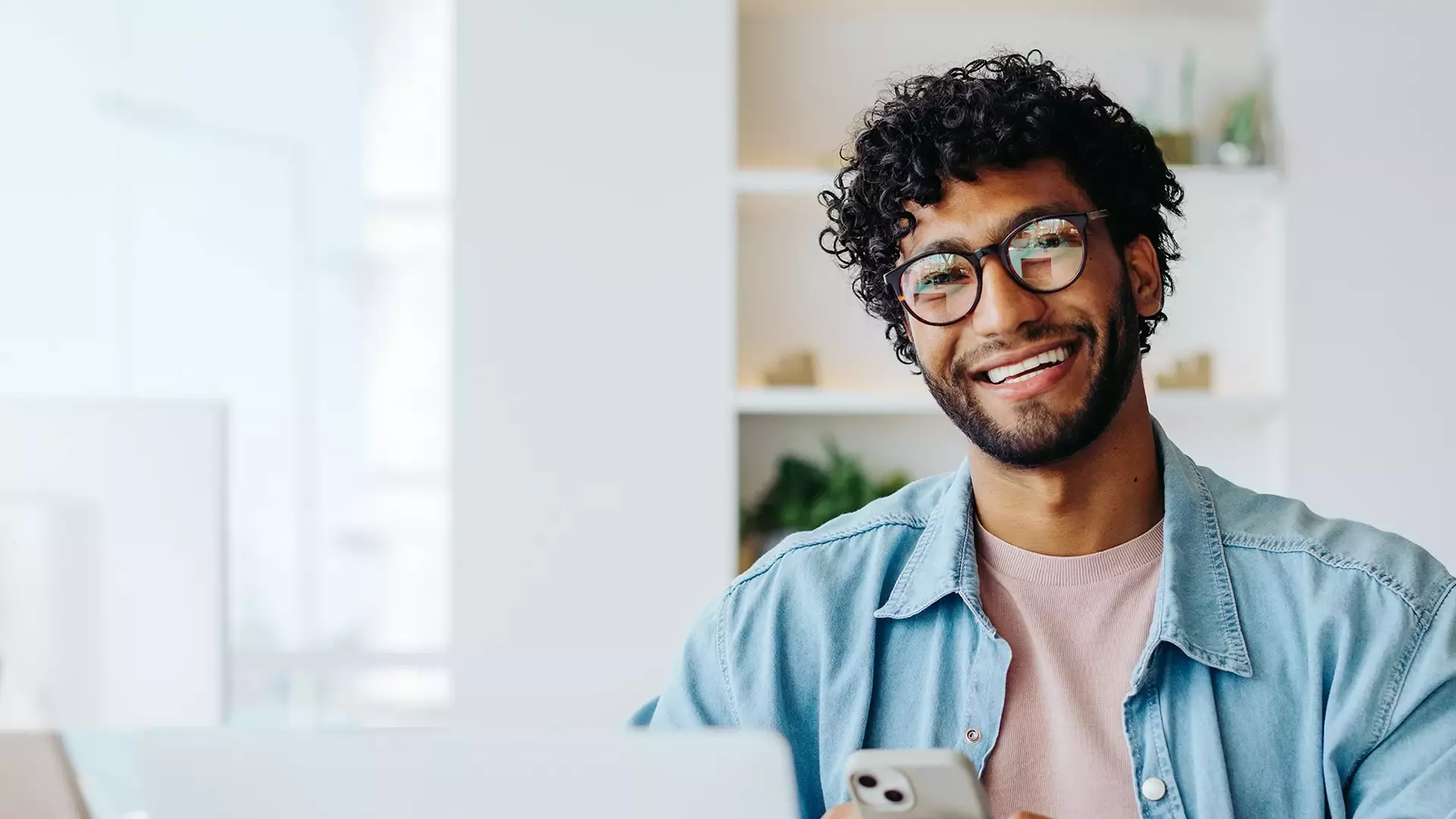 Een lachende persoon met een bril, die een smartphone vasthoudt.