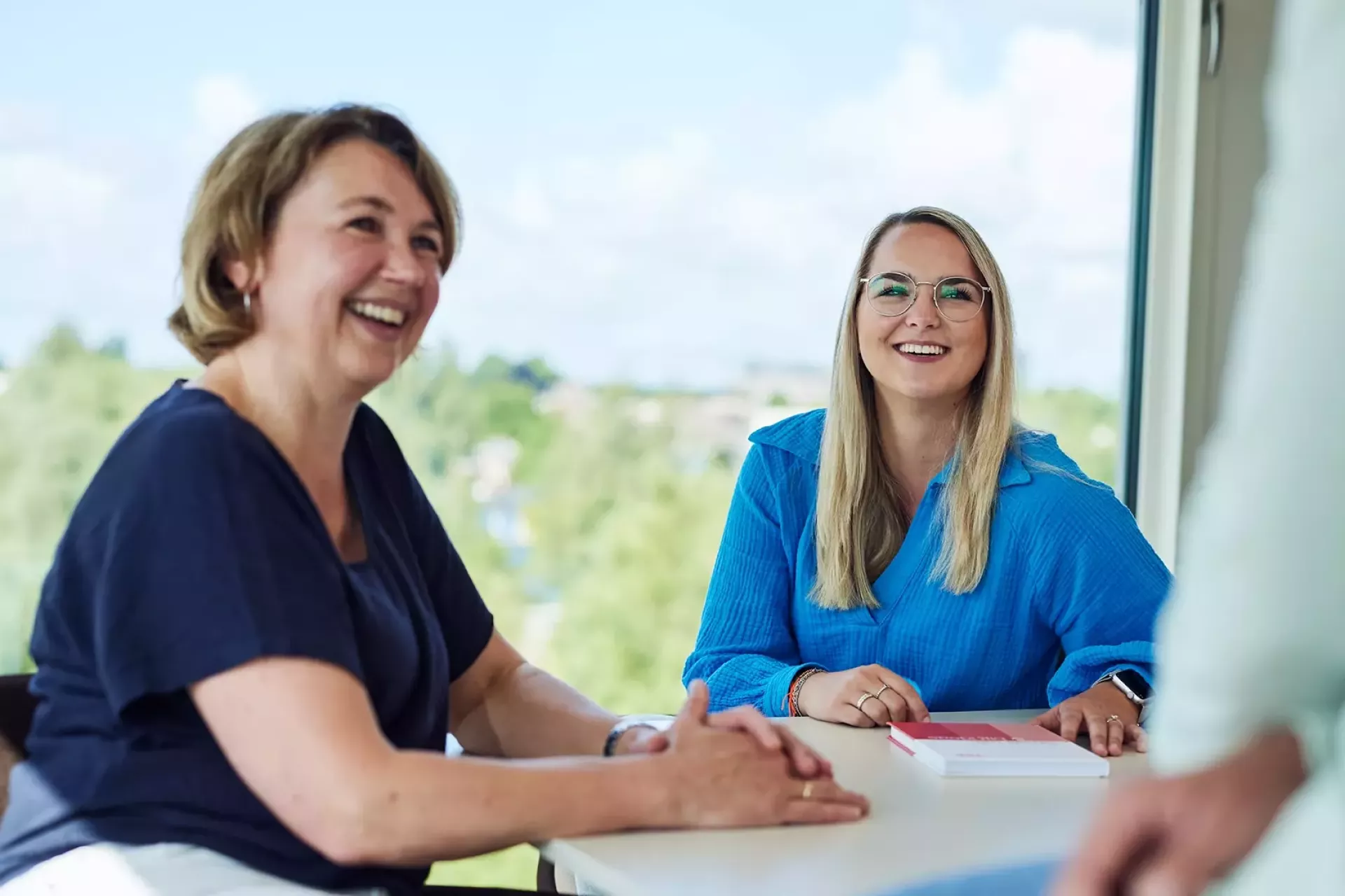 Twee vrouwen glimlachen tijdens een gesprek aan tafel.