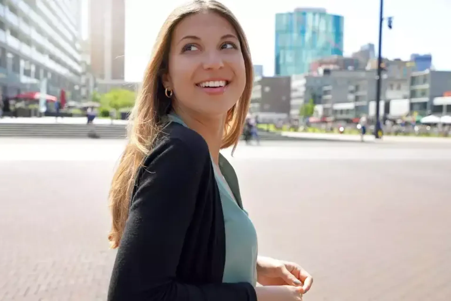 Vrouw glimlacht terwijl ze buiten in de stad loopt.