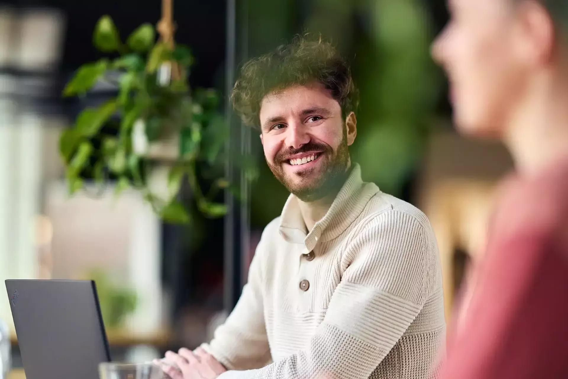 Een man glimlacht terwijl hij achter een laptop zit.