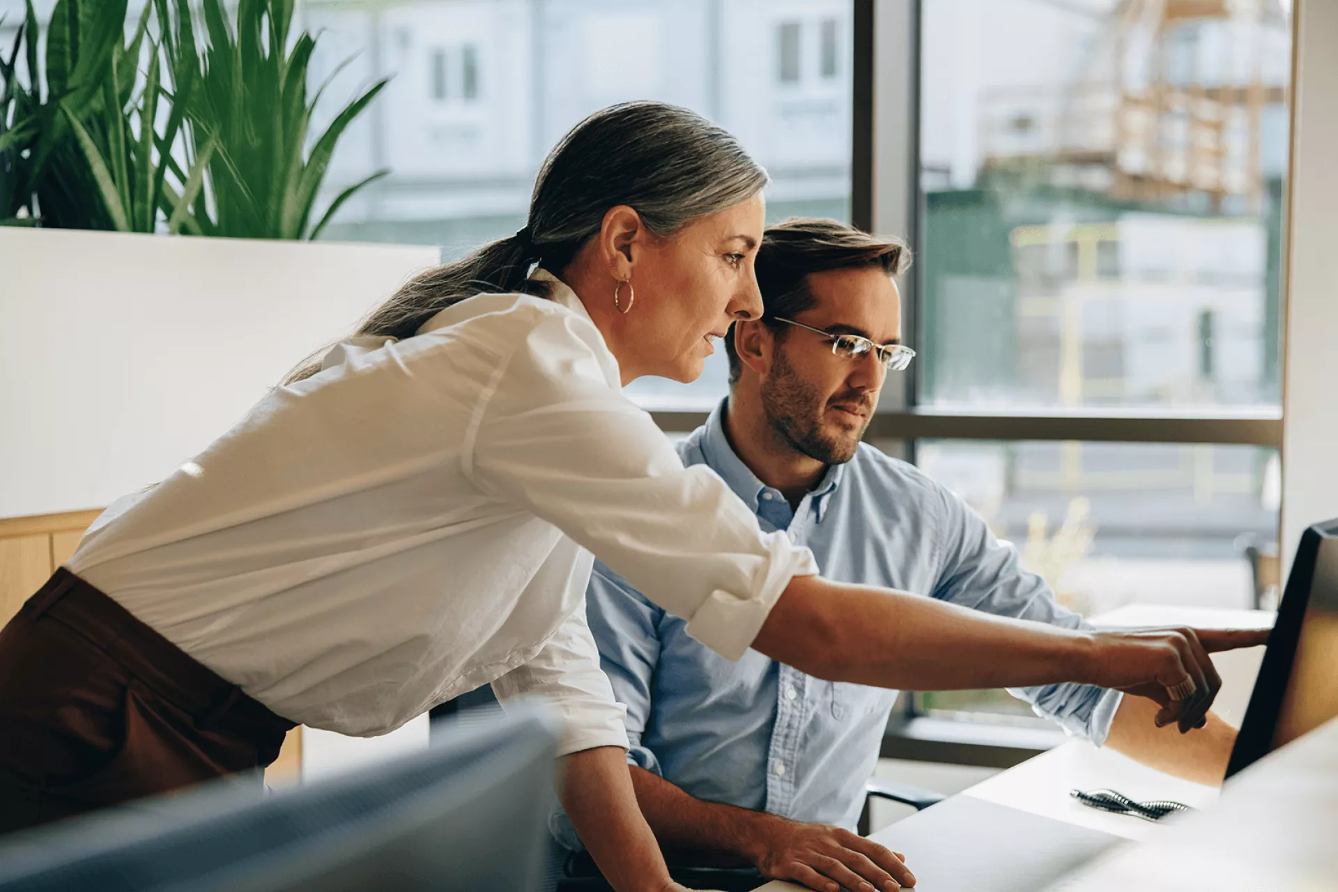 Twee collega's werken samen aan een computer in een kantoorruimte.