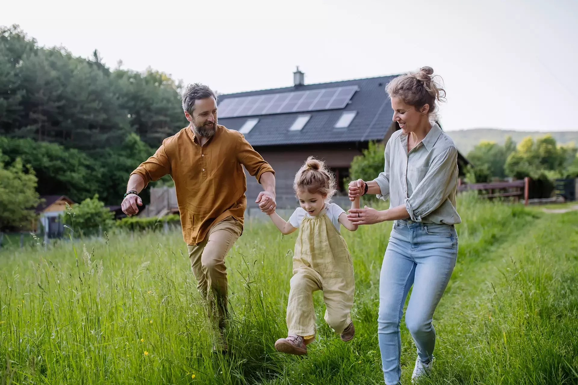 Een gezin dat samen door een grasveld loopt bij een huis met zonnepanelen.