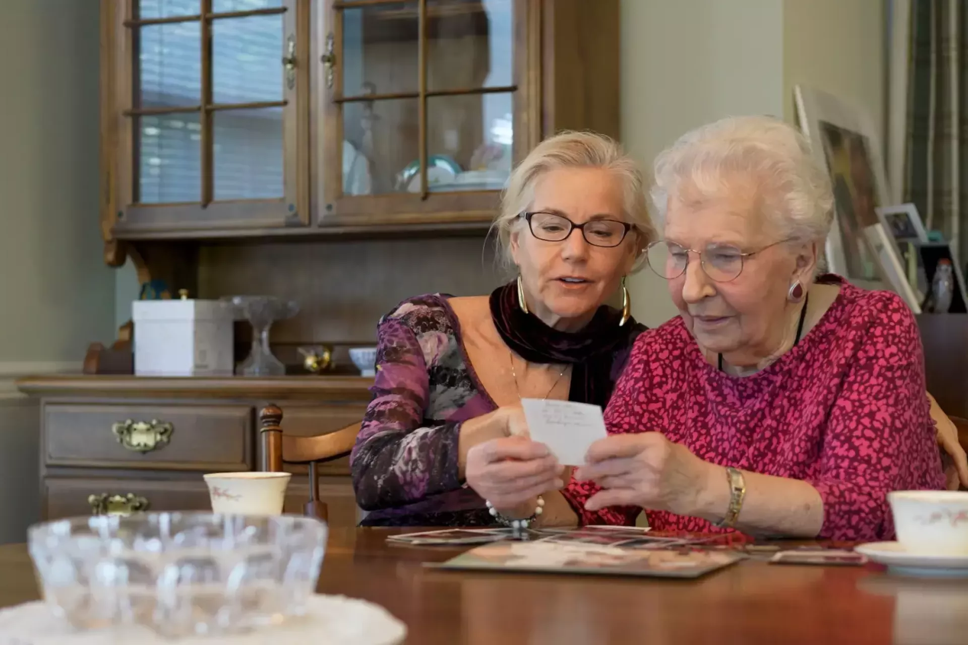 Twee oudere vrouwen bekijken samen een fotoalbum aan een tafel.