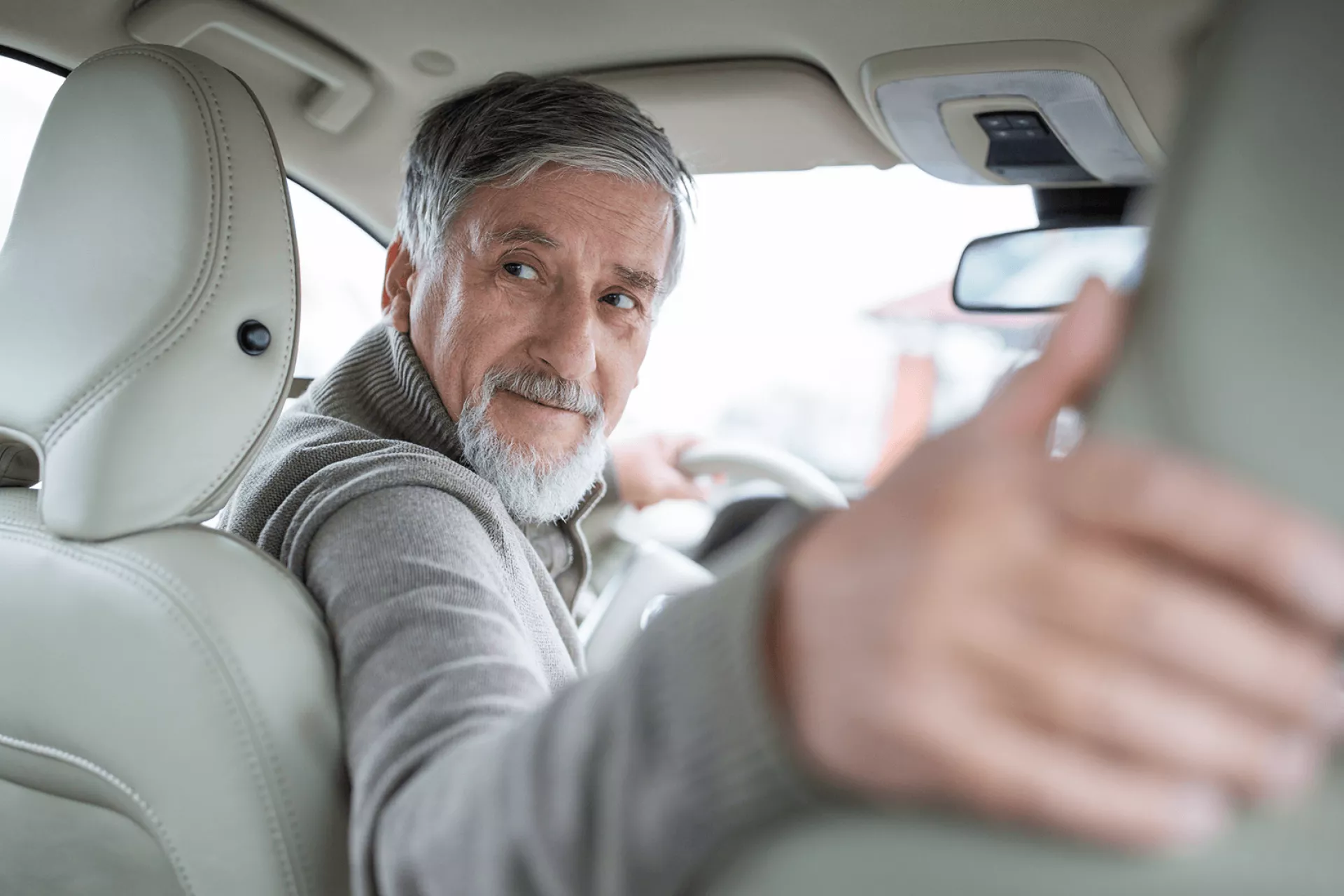 Een oudere man kijkt achterom terwijl hij in een auto zit.