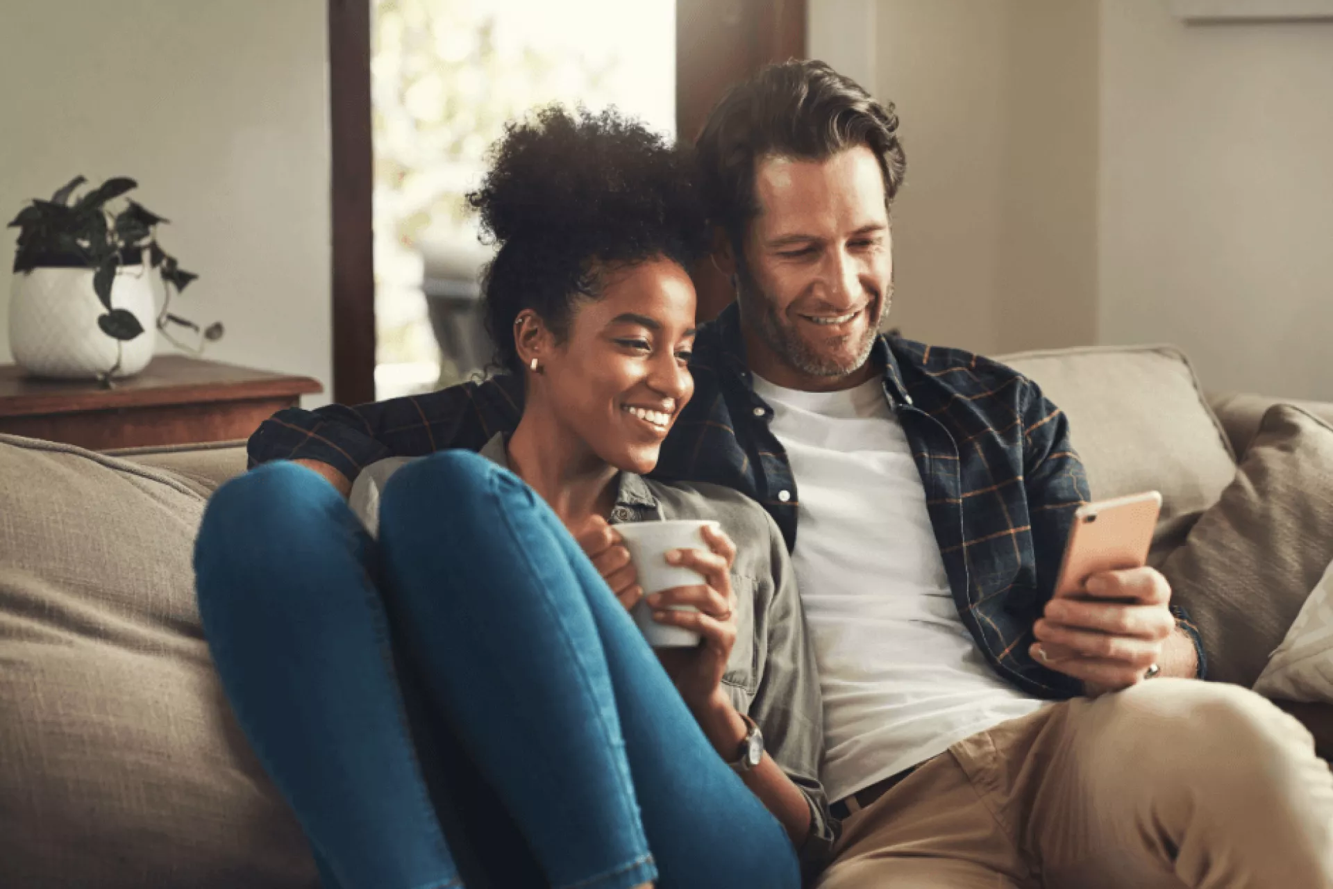 Een stel zit ontspannen op de bank terwijl ze samen naar een smartphone kijken.