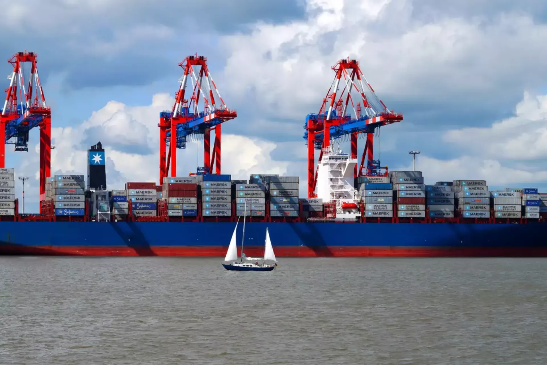Een groot containerschip in de haven met een zeilboot op de voorgrond.