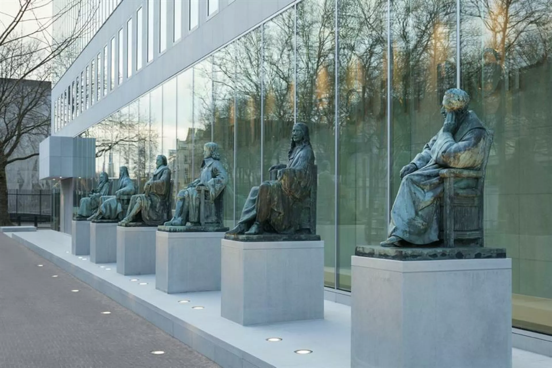 Rij van standbeelden voor een modern glazen gebouw.