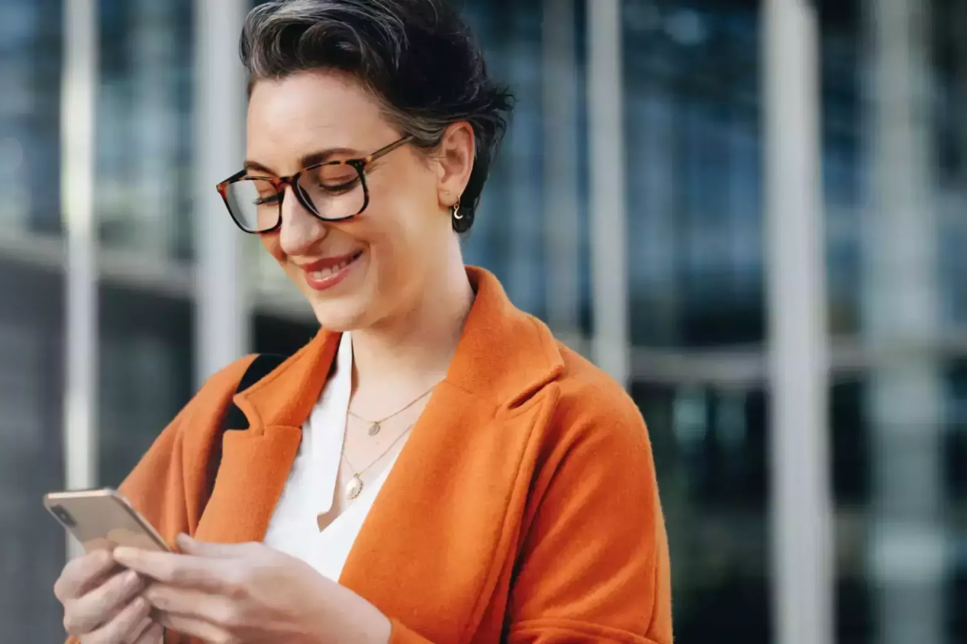 Vrouw glimlacht terwijl ze op haar telefoon kijkt.