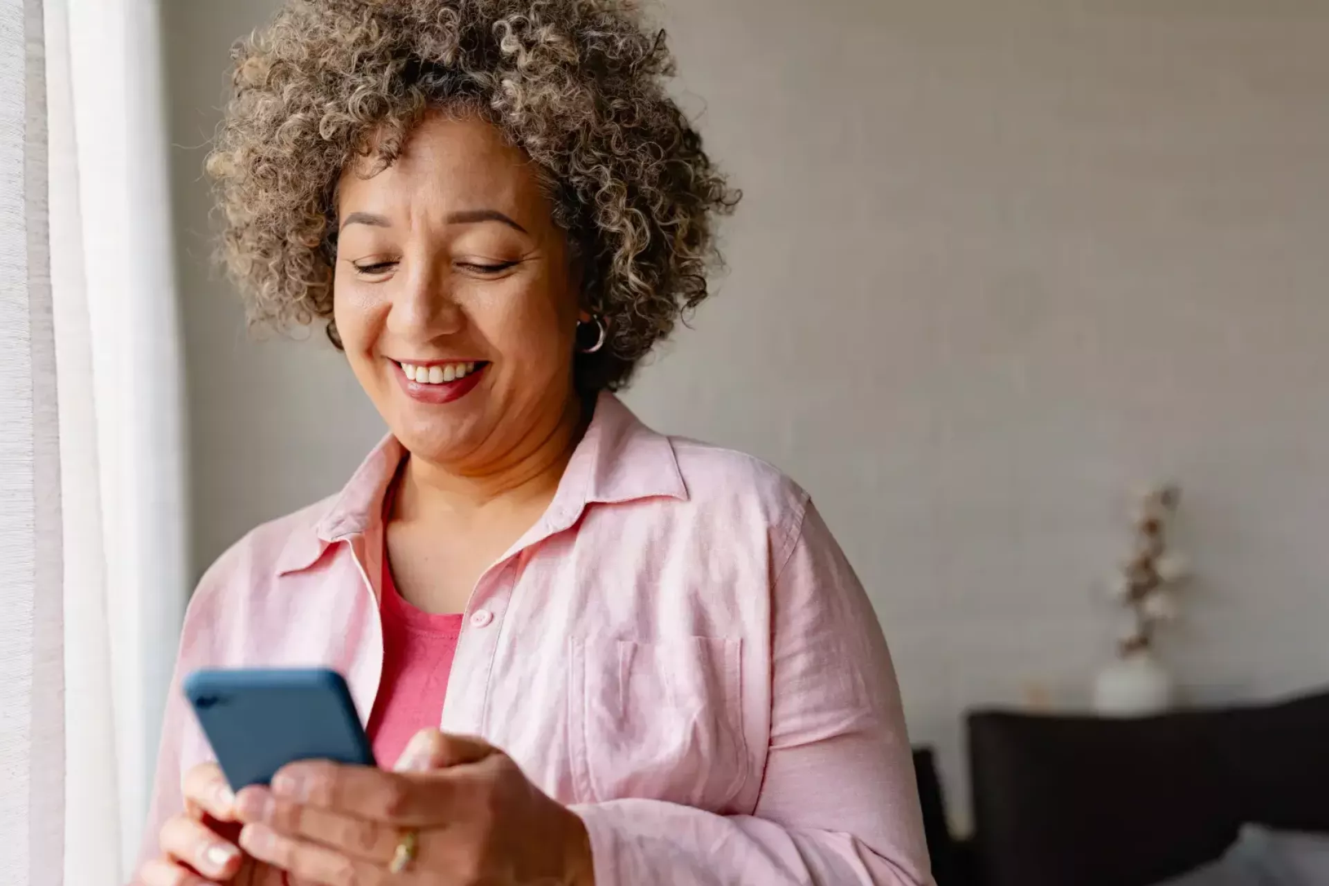 Vrouw glimlacht terwijl ze haar telefoon gebruikt bij een raam.